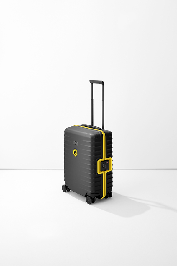 Black S23 trolley with yellow accents and extendable handle, stands on a white base. The BVB logo can be seen on the side of the case, as well as a TITAN logo. An integrated combination lock is also visible.