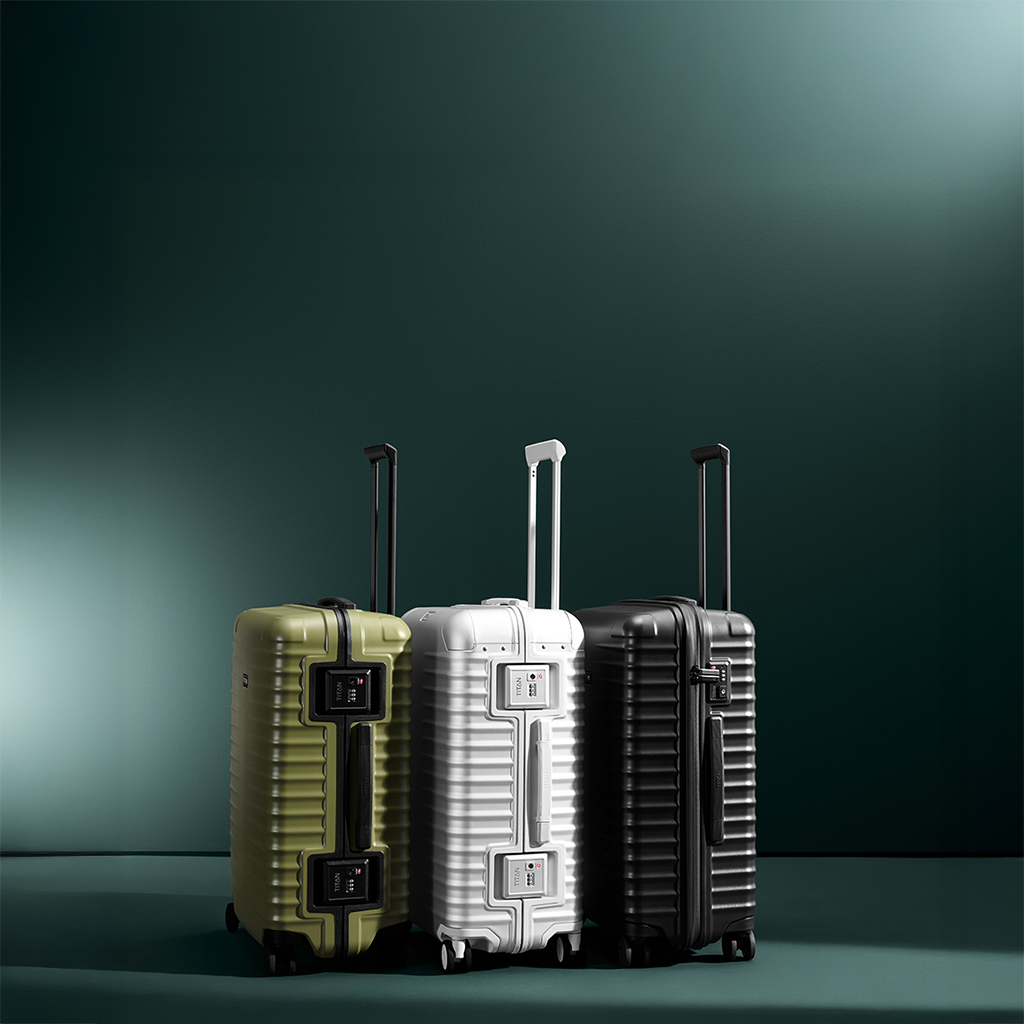 Tres maletas de distintos colores, una al lado de la otra: verde oliva, blanca y negra. Tienen asas telescópicas extraíbles y cerraduras de combinación. La superficie de las maletas es estriada. El fondo es verde oscuro.