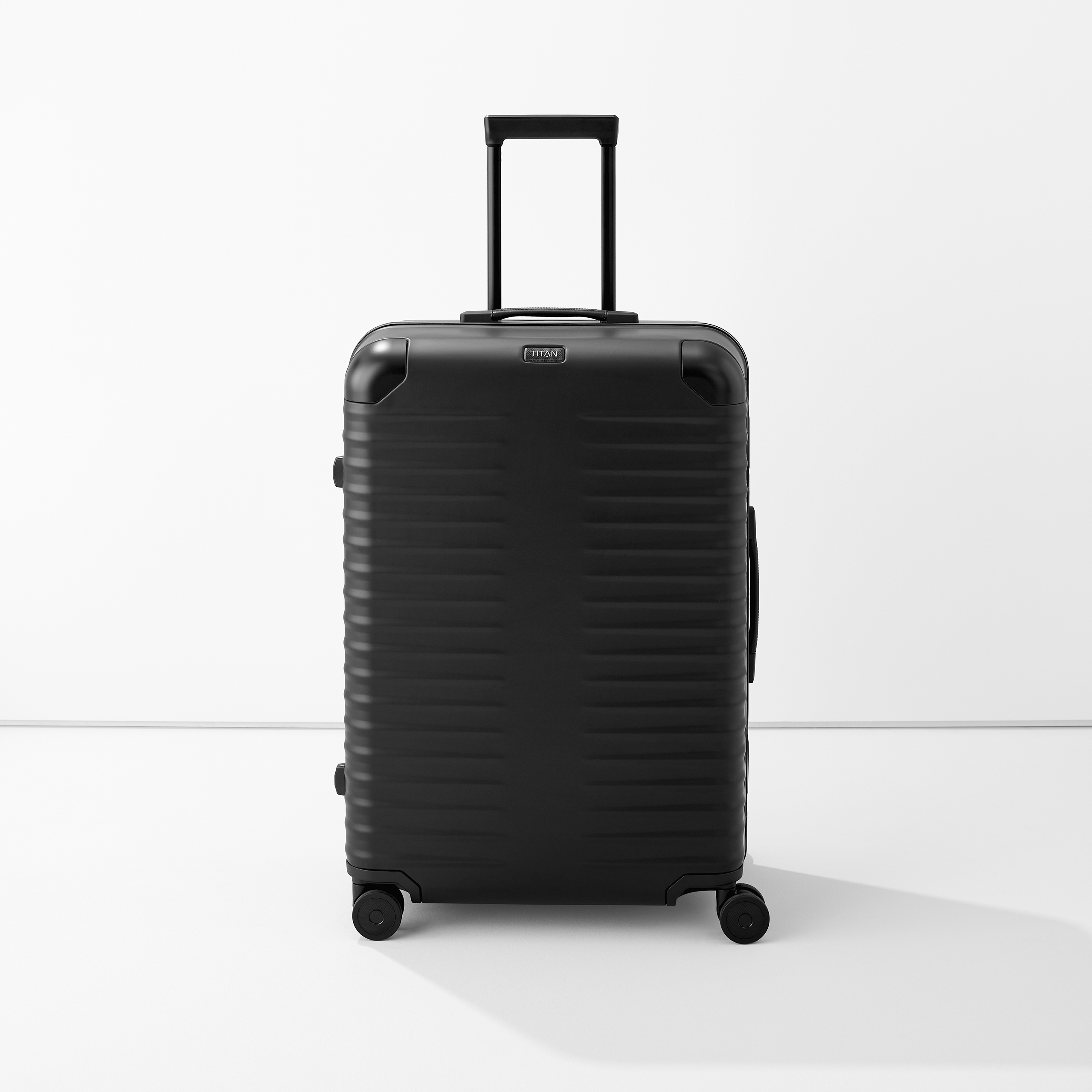 Valise noire à coque dure sur quatre roulettes avec poignée télescopique, autonome sur fond blanc