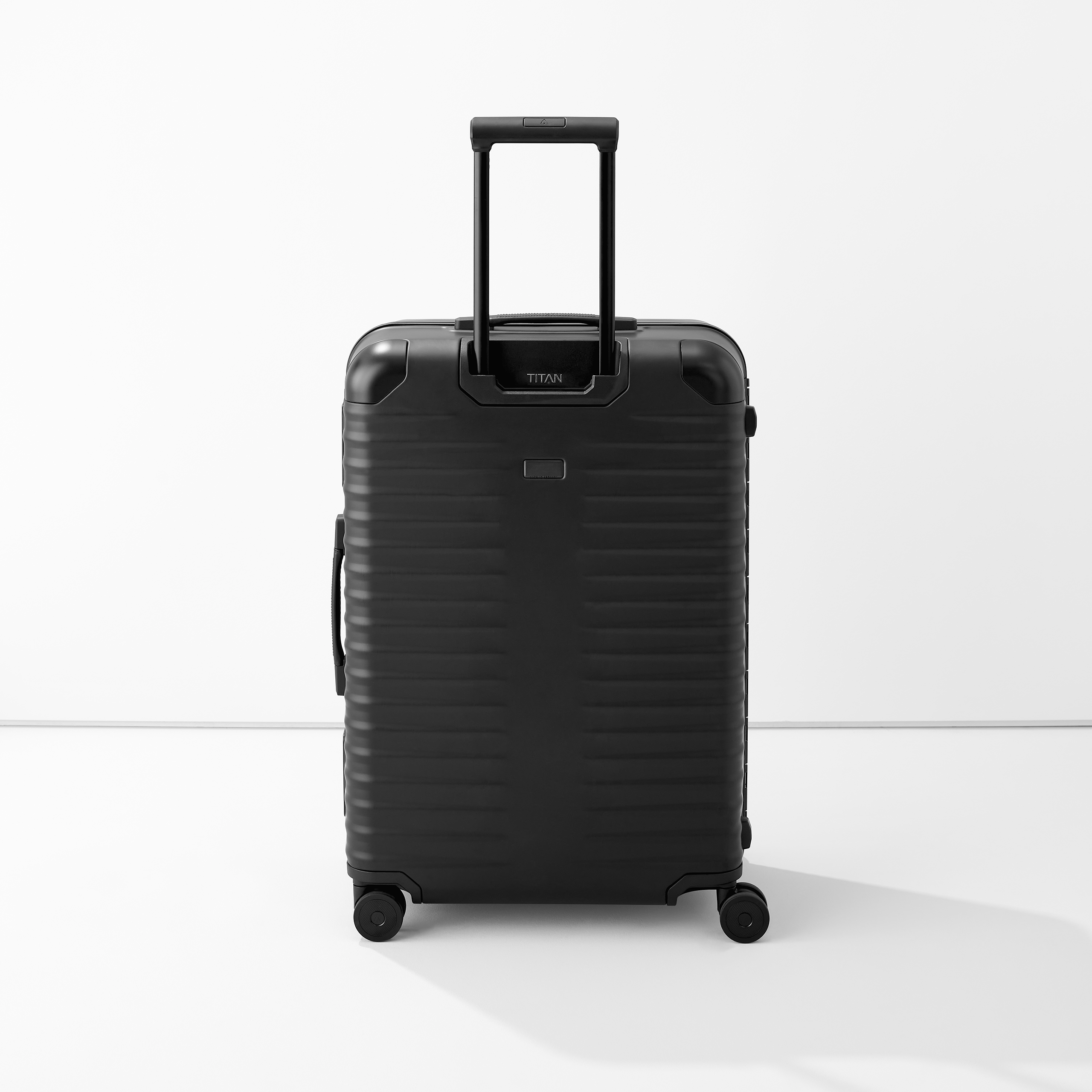 Valise noire moderne à coque dure avec poignée télescopique et quatre roulettes, debout sur fond blanc