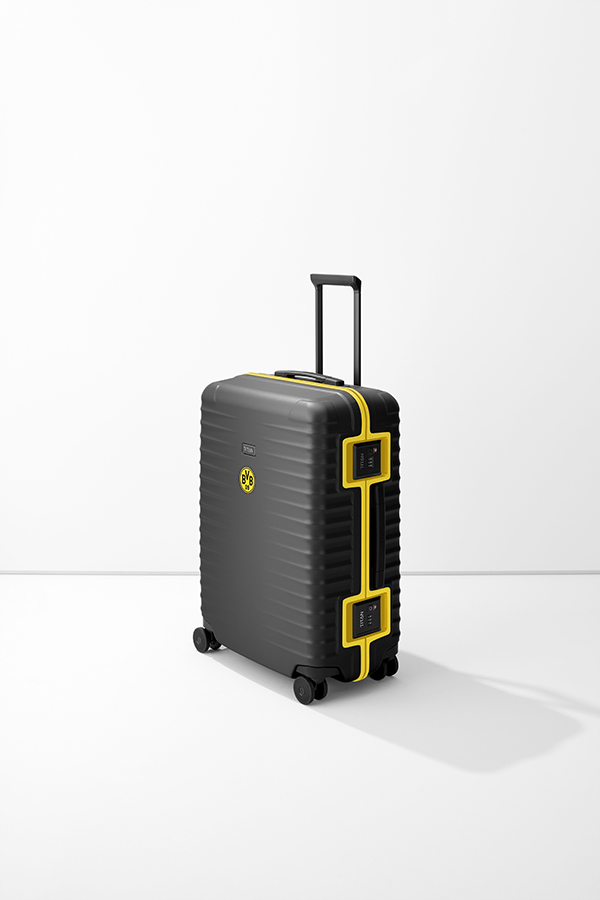 An M+ trolley from TITAN in black and yellow stands against a white background. The case has an extendable handle and four wheels. A BVB logo can be seen on the left-hand side. Two TSA locks are attached on the right-hand side.